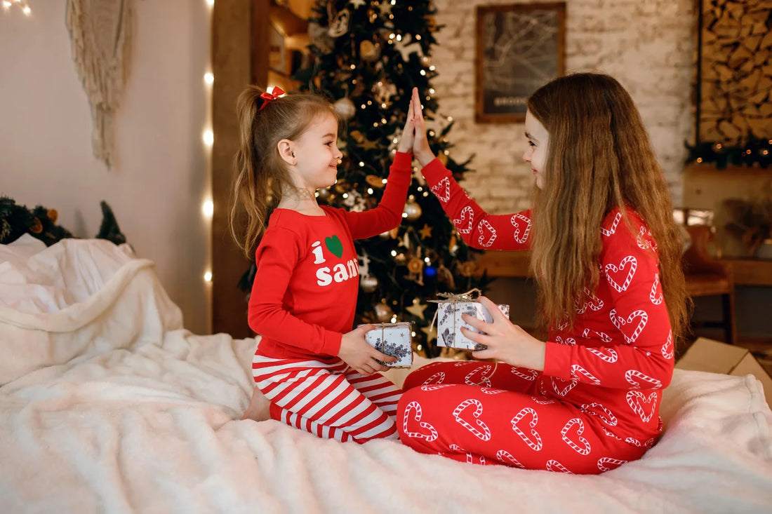 Deux sœurs en pyjama de Noël rouge sur un lit devant le sapin