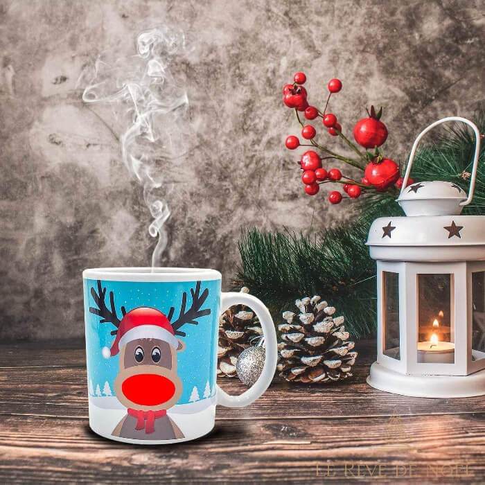 Mug blanc à motif renne au nez rouge et bonnet de Noël, vapeur montant de la tasse sur une table en bois