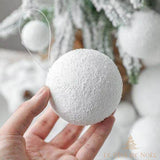 Boule de Noël enneigée tenue en main, texture givrée, devant un sapin enneigé