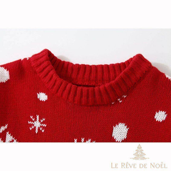 Col côtelé d'un pull de Noël bébé rouge en gros plan, pois et flocons de neige blancs tricotés