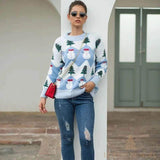 Femme portant un pull bleu clair à motif bonhommes de neige et sapins, jean déchiré, sac rouge