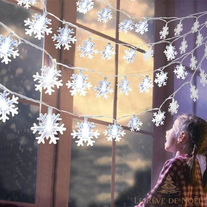 Guirlande lumineuse en flocons de neige blancs devant une fenêtre, enfant qui l'observe