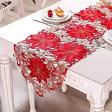 Gros plan sur un chemin de table brodé rouge et doré à fleurs de poinsettia ajourées, table blanche et assiette de fête