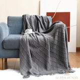 Plaid de Noël gris à motif losanges drapé sur un fauteuil bleu, tasse de café, tapis blanc