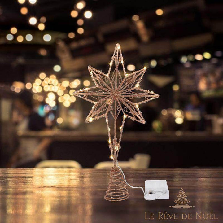Cimier étoile doré rosé allumé posé sur une table en bois, guirlandes lumineuses en arrière-plan