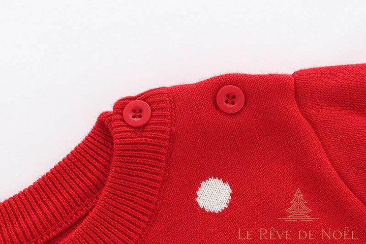 Gros plan sur les boutons rouges à l'épaule du pull de Noël enfant rouge à pois blancs
