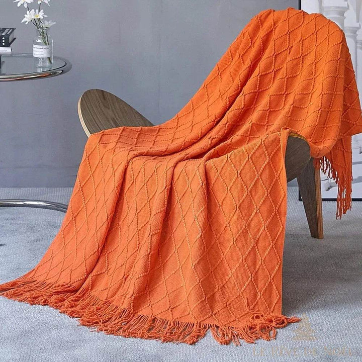 Plaid de Noël orange drapé sur une chaise en bois, petite table avec fleurs blanches en fond