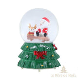 Boule à neige avec Père Noël et renne assis sur une bûche, socle vert en forme de sapin