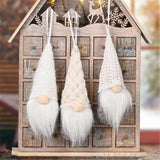 Trois lutins en tricot blanc suspendus devant une maison en bois façon calendrier de l'Avent