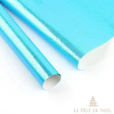 Deux rouleaux de papier cadeau brillant bleu turquoise, feuille dépliée en arrière-plan