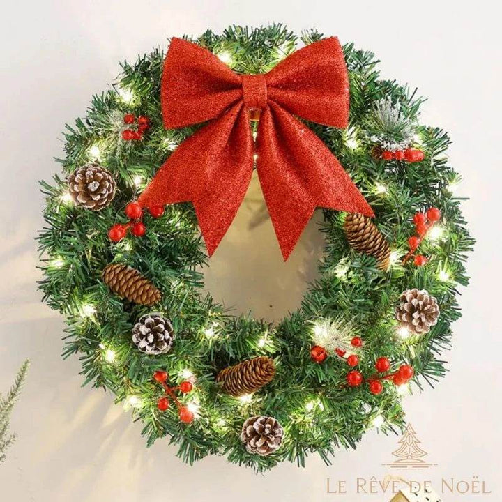 Couronne de Noël avec guirlande lumineuse allumée et nœud rouge, accrochée au mur