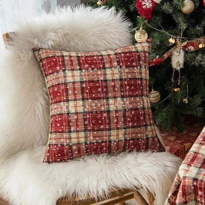 Housse de coussin tartan rouge à motifs flocons, posée sur un fauteuil moelleux blanc