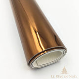 Papier cadeau métallisé marron cuivré brillant, enroulé en rouleau montrant l'envers blanc du papier