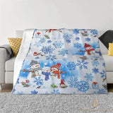 Plaid de Noël bleu et blanc posé sur un canapé, motif de flocons et bonhommes de neige