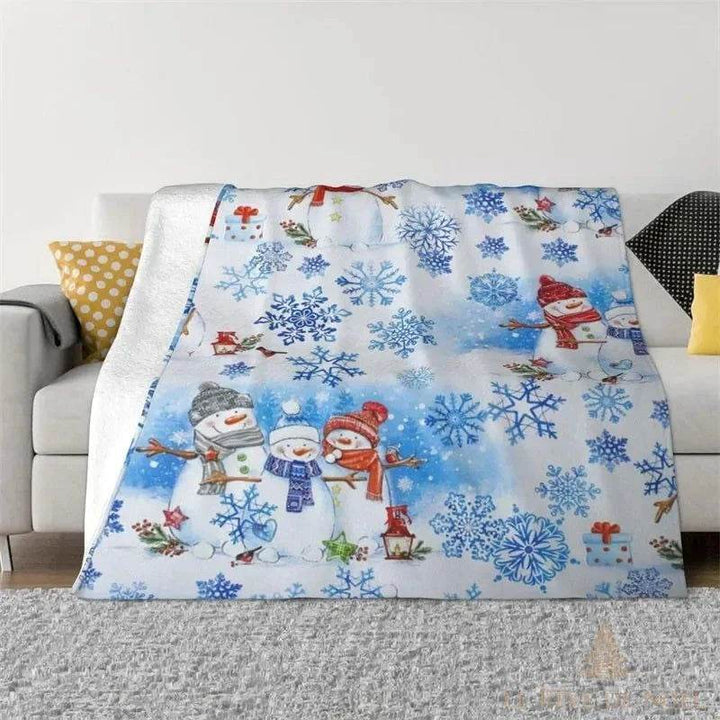 Plaid de Noël bleu et blanc posé sur un canapé, motif de flocons et bonhommes de neige