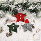 Trois étoiles de Noël en feutrine rouge, verte et grise, avec bonnet tricoté et boutons, sur la neige