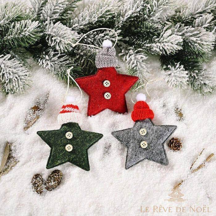 Trois étoiles de Noël en feutrine rouge, verte et grise, avec bonnet tricoté et boutons, sur la neige