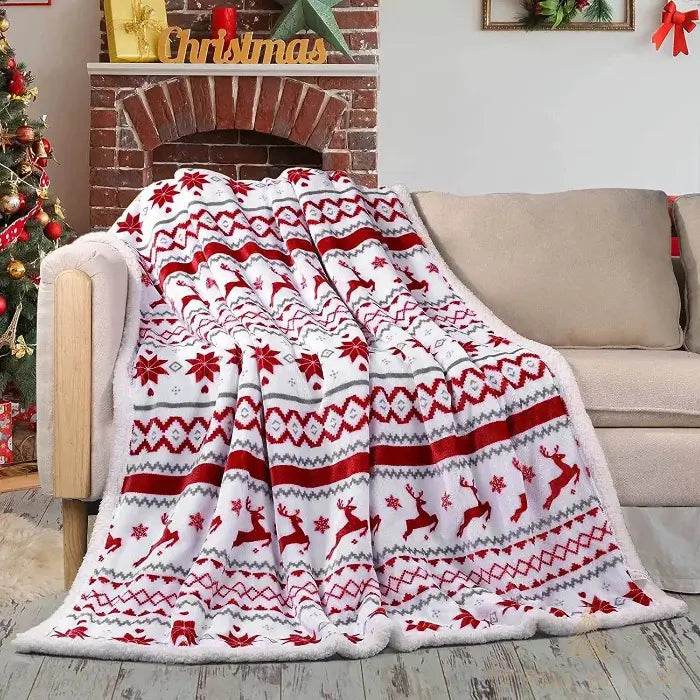Plaid polaire motifs rennes et flocons rouge et blanc, posé sur un fauteuil près d'une cheminée