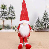 Lutin rouge à longue barbe blanche assis sur un petit tabouret devant des sapins enneigés