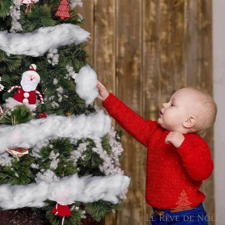 Enfant touchant de la neige artificielle posée sur les branches d'un sapin décoré