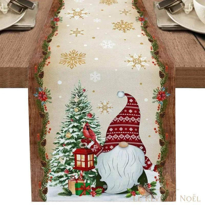 Même chemin de table beige à flocons dorés, avec grand gnome barbu au bonnet nordique rouge, lanterne et cadeau au sapin