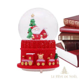 Boule à neige de Noël au Père Noël, posée sur une table à côté d'une pile de livres reliés rouges
