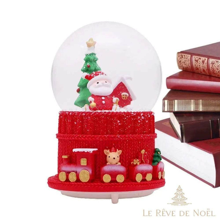 Boule à neige de Noël au Père Noël, posée sur une table à côté d'une pile de livres reliés rouges