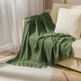 Plaid de Noël vert drapé sur un canapé crème, coussin blanc moelleux, rideaux voilage en fond