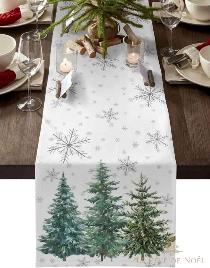 Chemin de table blanc à flocons argentés et sapins peints, dressé avec bougies, verres à vin et branches de sapin