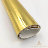 Papier cadeau métallisé doré brillant, enroulé en rouleau montrant l'envers blanc du papier