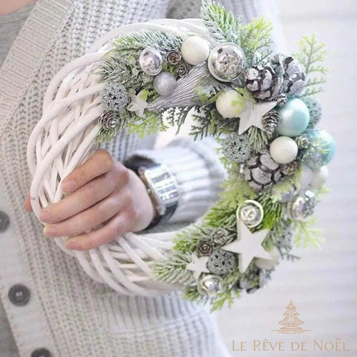 Couronne en osier blanc décorée de boules argentées, pommes de pin et branches, tenue en main