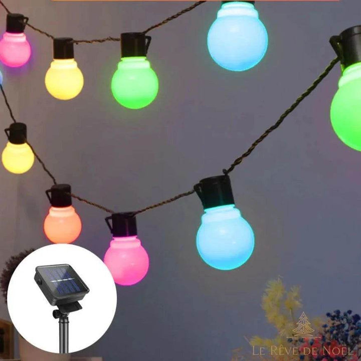 Guirlande solaire à ampoules multicolores allumées la nuit sur un mur, panneau solaire en médaillon