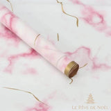 Rouleau de papier cadeau marbré rose et blanc, posé en diagonale avec des rubans dorés bouclés