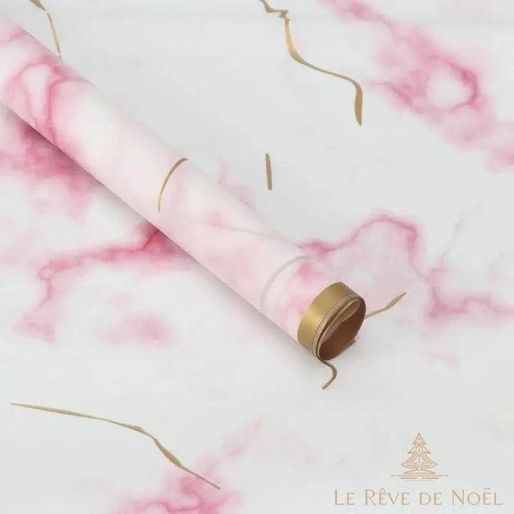 Rouleau de papier cadeau marbré rose et blanc, posé en diagonale avec des rubans dorés bouclés