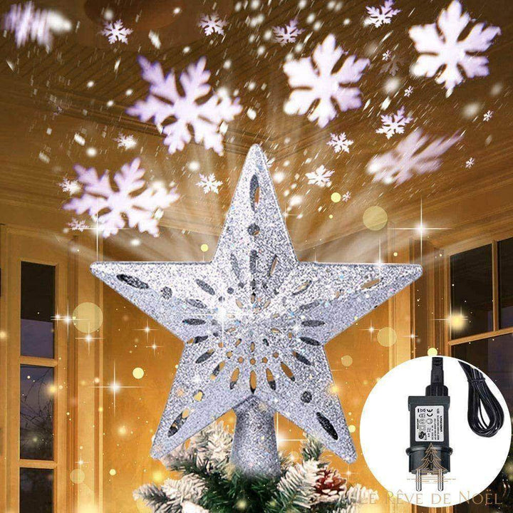 Cimier étoile argentée pailletée sur un sapin, projetant des flocons de neige lumineux au plafond dans une pièce sombre