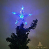 Cimier étoile à LED bleues allumé au sommet d'un sapin, pièce sombre en arrière-plan