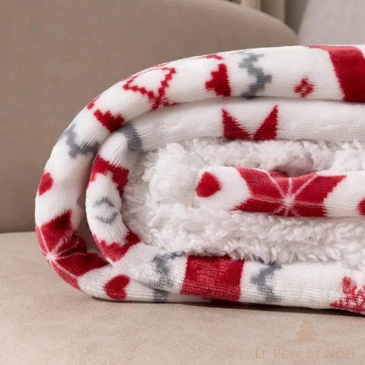 Gros plan sur le plaid polaire roulé, motifs flocons rouges et envers moelleux blanc