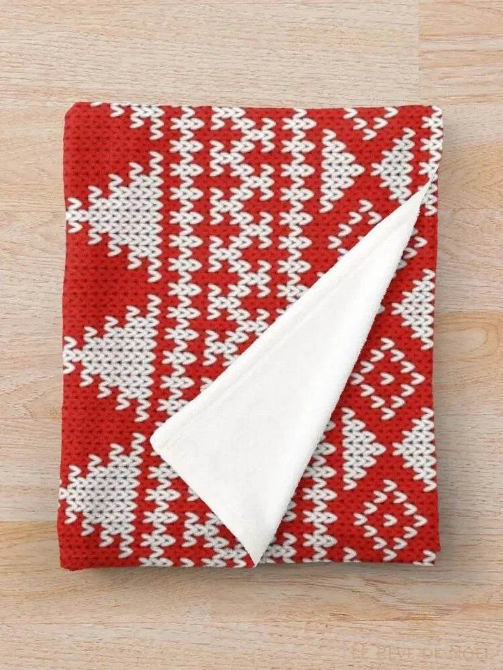 Plaid tricoté rouge à motifs flocons blancs, plié avec un coin replié montrant l'envers polaire