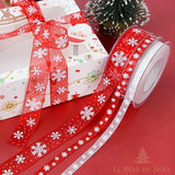 Nœud en ruban organza rouge à flocons sur un coffret cadeau, bobine de ruban à côté