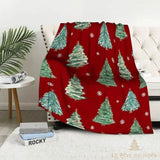 Plaid de Noël rouge à sapins verts illustrés, posé sur un fauteuil capitonné blanc