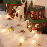 Neige artificielle en couche sous des boîtes cadeaux, boules de Noël et un renne blanc miniature