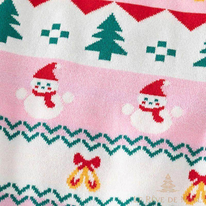 Motif tricoté en gros plan sur le pull rose : sapins, bonhomme de neige et clochettes