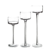 Trois bougeoirs en verre transparent de hauteurs différentes, alignés sur fond blanc