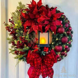 Couronne de Noël rouge avec lanterne lumineuse, boules et fleurs rouges, sur une porte