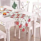Chemin de table blanc brodé de fleurs de poinsettia rouges, bords festonnés, sur table blanche avec chaises et cactus