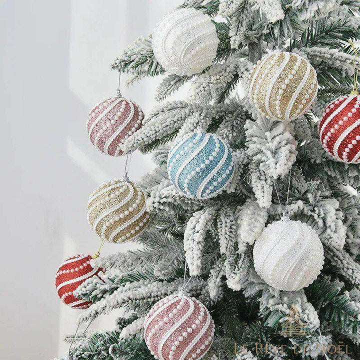Gros plan sur des boules de Noël perlées multicolores accrochées aux branches d'un sapin enneigé
