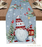 Chemin de table bleu-gris à grand gnome barbu et bonnet rouge, sur table en bois avec sapins et lanterne rouge allumée