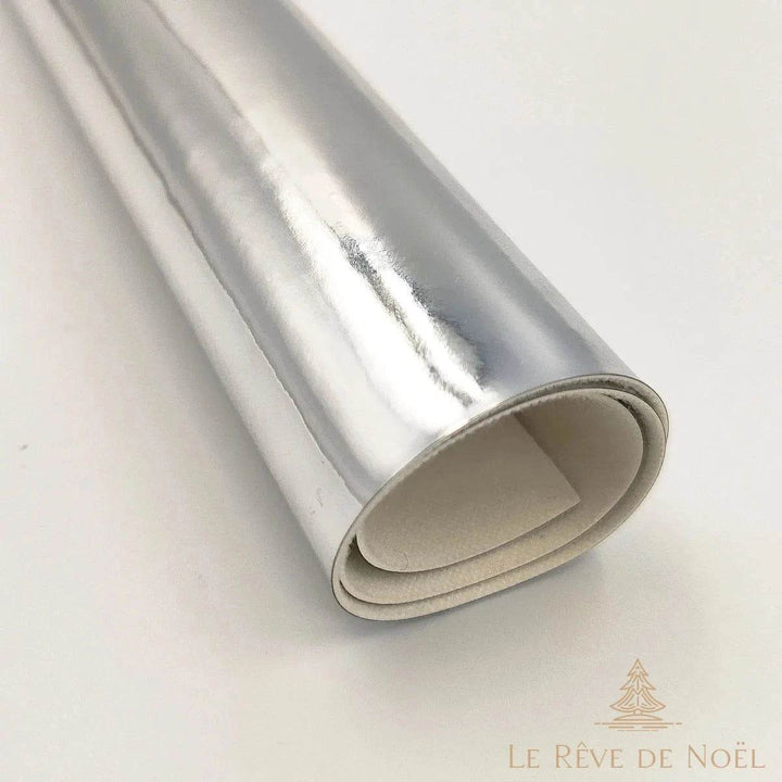 Papier cadeau métallisé argenté brillant, enroulé en rouleau montrant l'envers blanc du papier