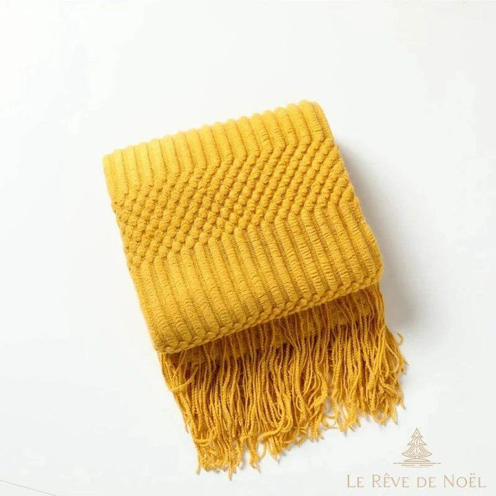Plaid de Noël en maille jaune moutarde plié, texture en chevrons et picots, franges visibles