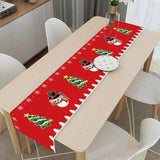 Chemin de table rouge à motif bonhommes de neige et sapins, posé en long sur une table en bois entre chaises blanches